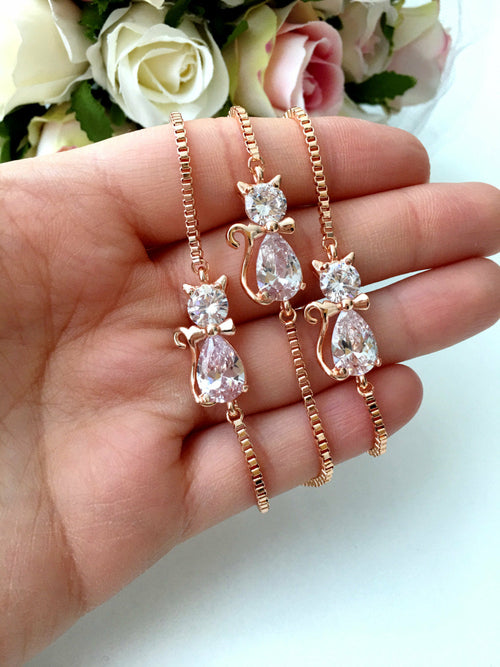 Rose gold cat-shaped earrings with clear gemstones held in a hand against a floral background.