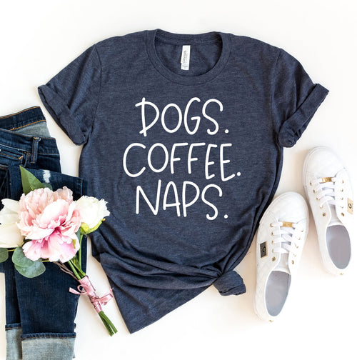 Navy blue t-shirt with 'DOGS. COFFEE. NAPS.' text, paired with jeans, sneakers, and flowers on a white background.