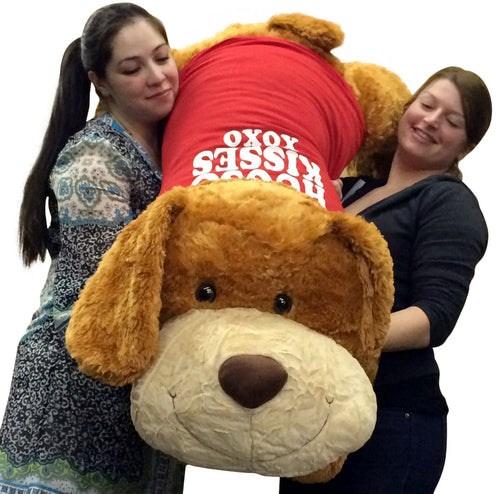 Two people holding a large plush dog with a red shirt on a white background