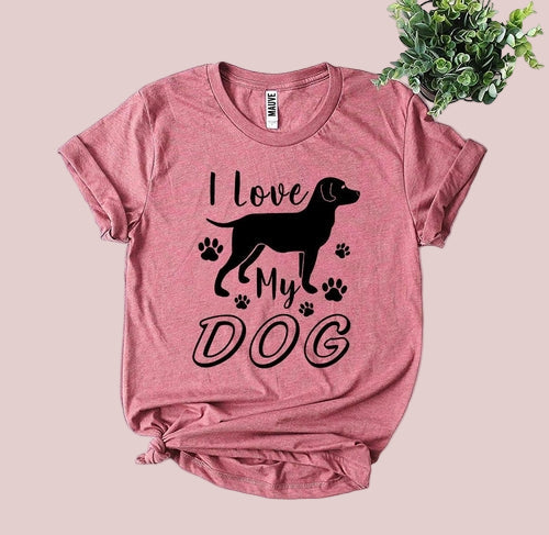 Pink t-shirt with 'I love my dog' graphic on a white wooden surface with a plant.