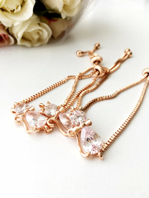 Rose gold necklace with pink gemstones on a white surface with flowers in the background